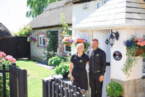 Photo of English Cottage Vacation co-hosts Laura and Nathan in front of Well Cottage, their luxury 18th-century thatched cottage in Dorset