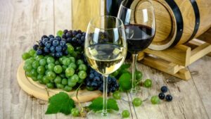Photo of glasses of red and white wine with bunches of grapes to illustrate the ideal holiday for wine lovers